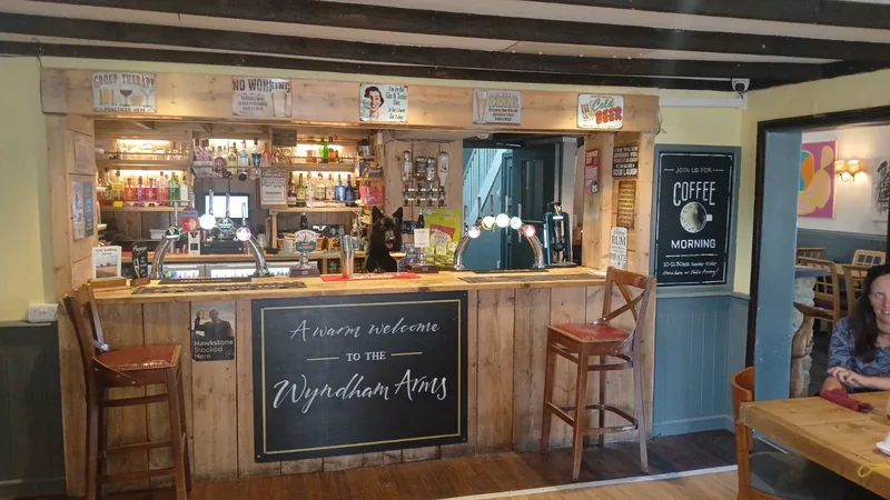 The bar at The Wyndham Arms seen across the room, with hand pumps, bar stools and Loki the pub dog behind the counter