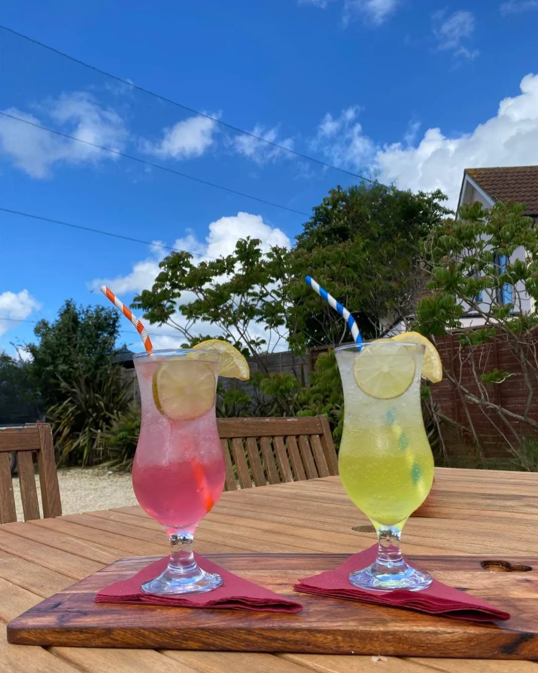 Two long drinks with lemon on a wooden table in the pub garden, blue sky above