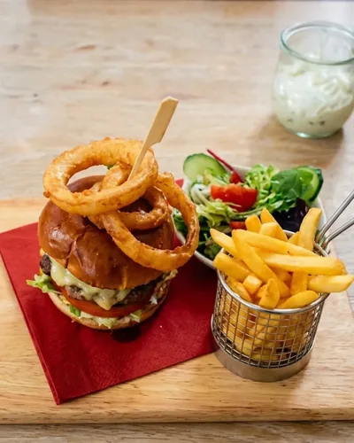 A burger with melted cheese, onion rings, fries and salad