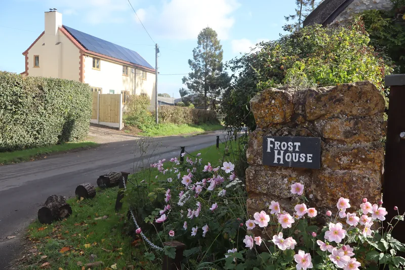 A stone gatepost and flowers beside a village road, with houses beyond