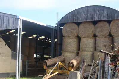 Round hay bales stacked under a farm barn roof