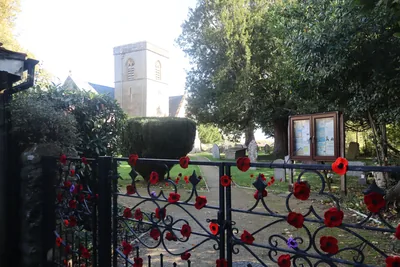 The village church tower seen through an iron gate hung with knitted poppies