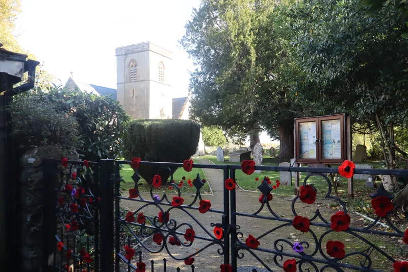 The village church tower seen through an iron gate hung with knitted poppies